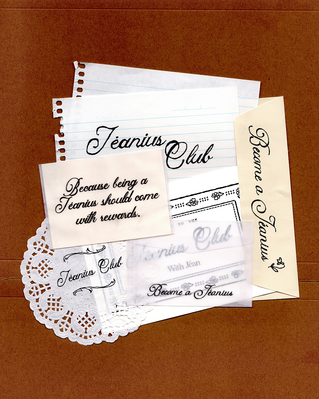 A flat-lay arrangement of vintage-style paper ephemera and stationery items on a brown textured background, including a lined notepad, cream cards with black script text reading 'Jeanius Club' and 'Become a Jeanius', a white lace doily, and a clear plastic sleeve. mobile