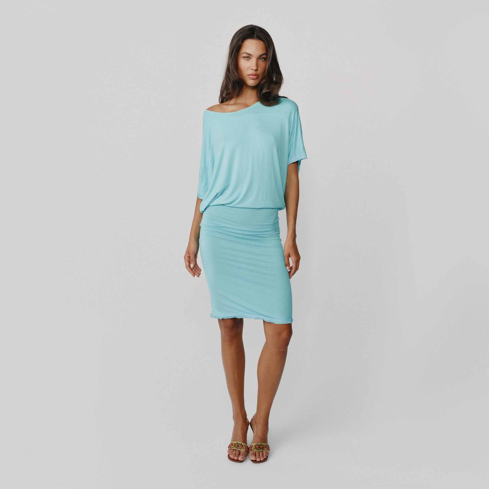 A woman modeling a light blue short sleeve knee length dress paired with leopard-print heeled sandals, against a solid light gray background.
